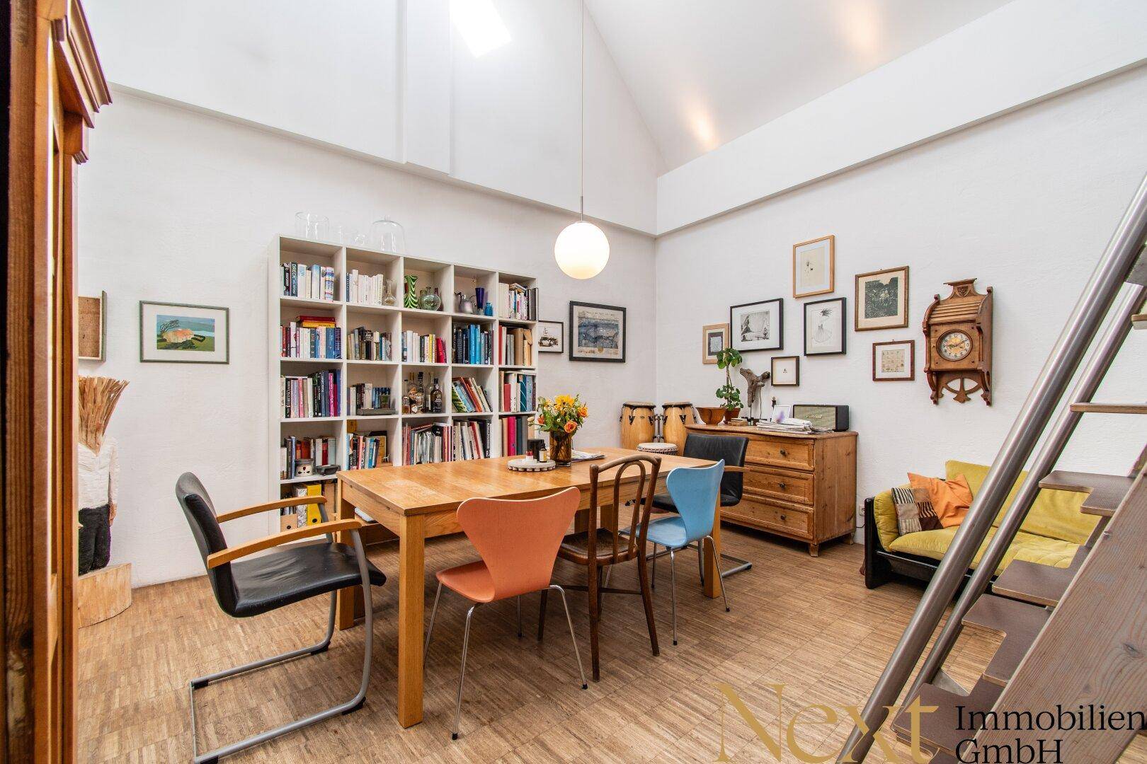 Geräumiger Essbereich mit Holztisch, bunten Stühlen und einem großen Bücherregal an der Wand.