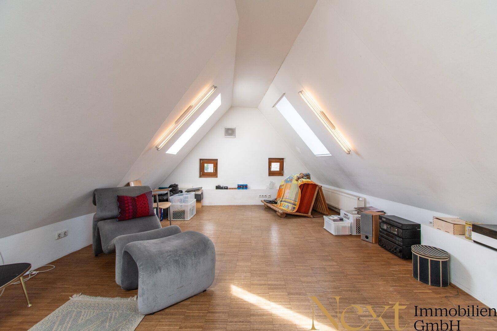 Helles Dachgeschoss mit schrägen Wänden, Dachfenstern und Holzboden, als Wohnraum genutzt.