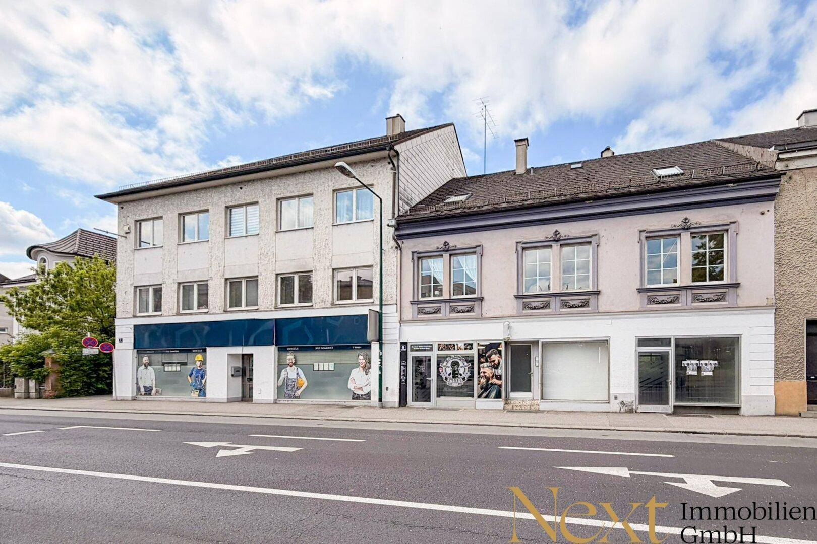 Ansicht von zwei Geschäftsgebäuden entlang einer Straße mit Schaufenstern und Obergeschossen.