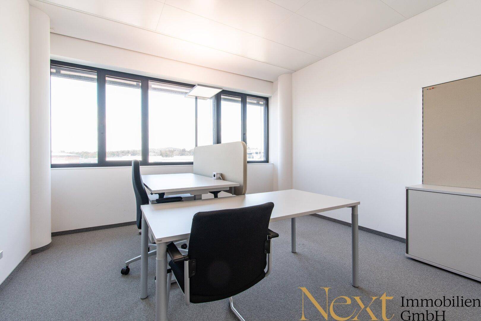 Helles Einzelbüro mit zwei Schreibtischen, ergonomischen Stühlen und weitem Ausblick.