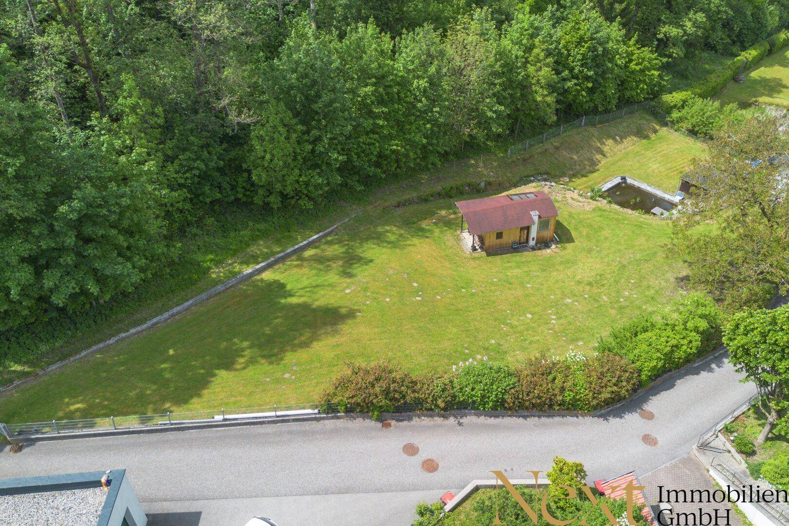 Weitläufiges Grundstück aus der Vogelperspektive mit einem kleinen Holzhaus und viel Grünfläche.