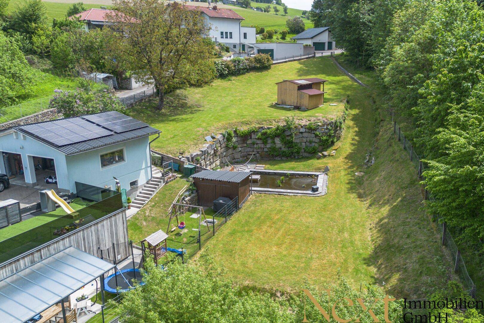 Luftaufnahme eines Hauses mit Solaranlage, Garten, Teich, Spielplatz und Trampolin.