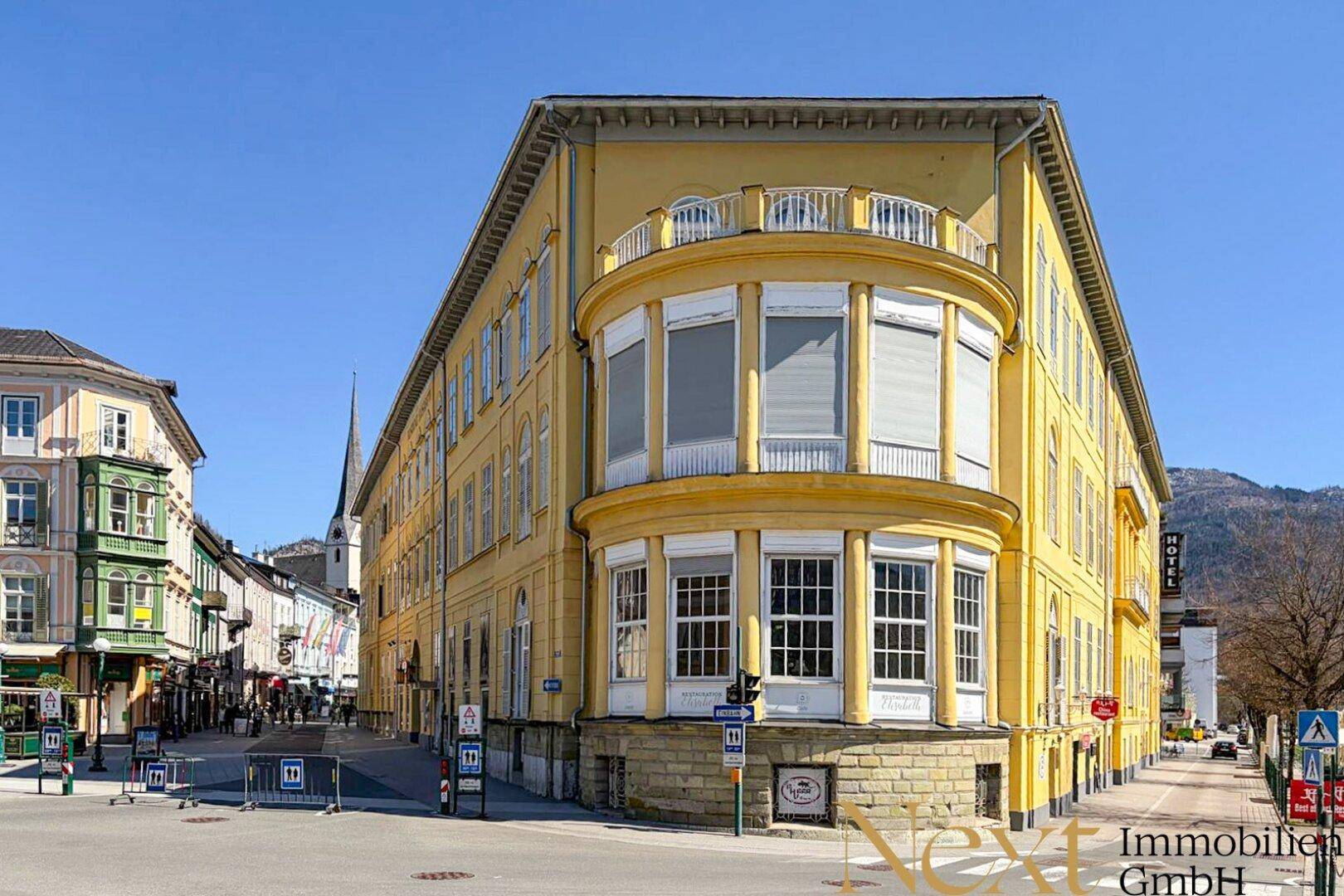 Historisches Eckgebäude mit runder Fassade, Balkonen und großen Fenstern an einer belebten Straße.