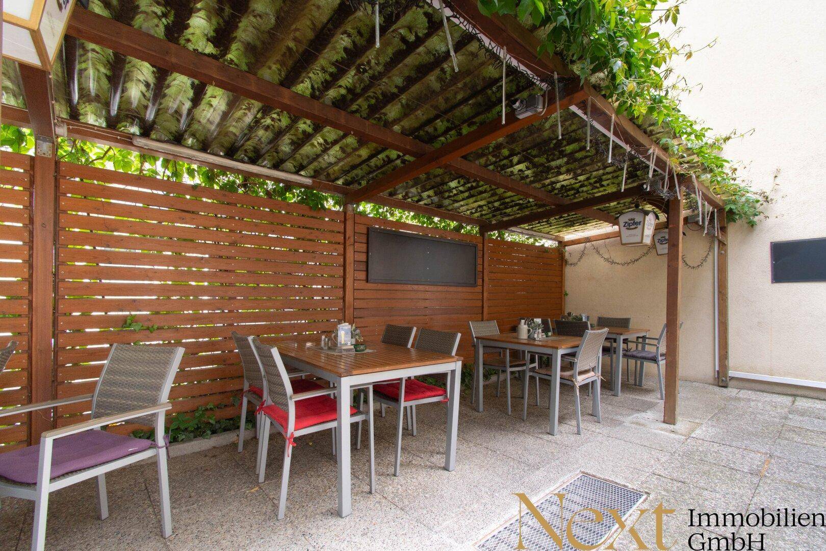 Überdachte Terrasse mit Holztischen und Sichtschutzwänden.