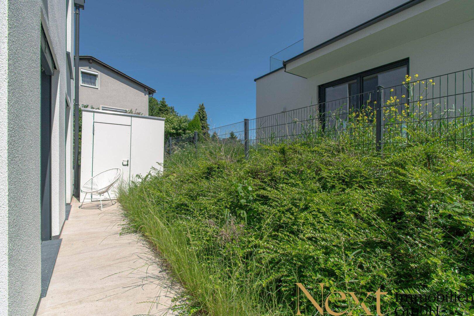 Außenbereich mit gepflastertem Weg, Grünfläche und Gartenhaus.