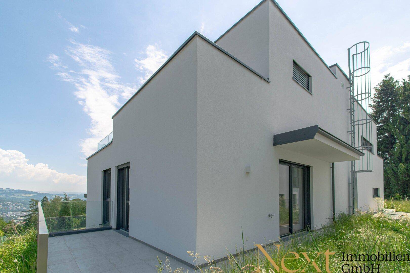 Moderne Gebäudeseite mit einer gefliesten Terrasse und weitem Blick in die grüne Landschaft.