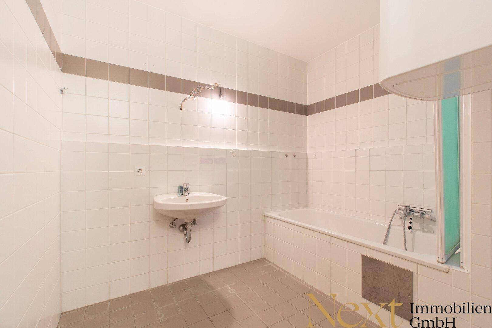 Badezimmer mit weißen Fliesen, Waschbecken und Badewanne mit Duschabtrennung, funktional und hell.