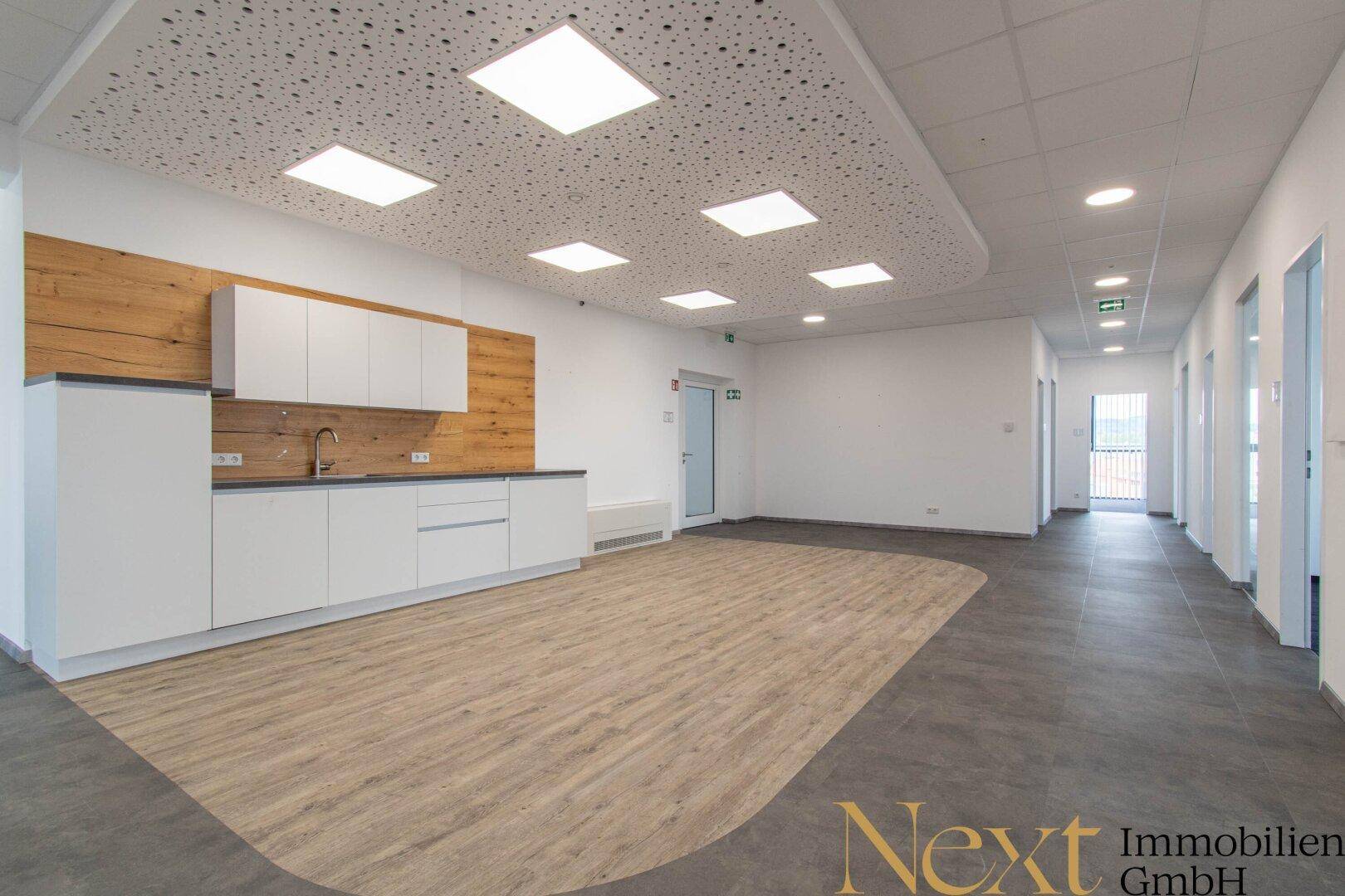 Geräumige Teeküche mit hellem Boden, weißen Schränken und Holzdetails in einem modernen Büro.