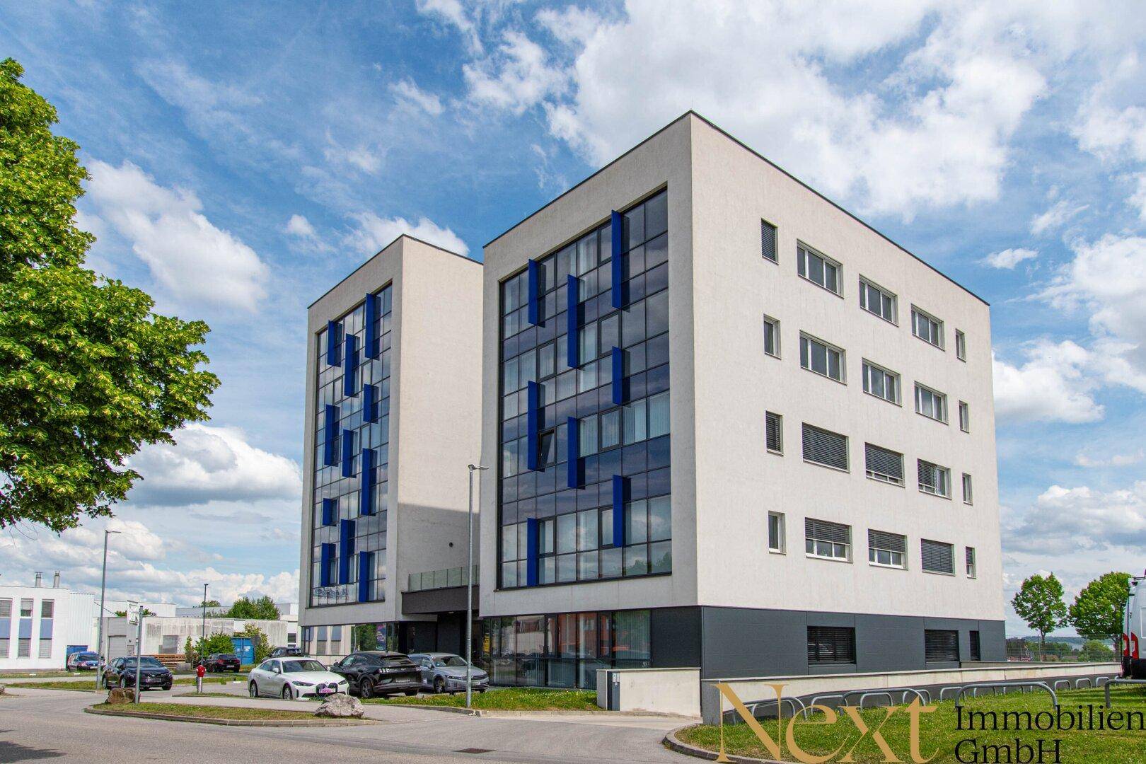 Zwei moderne Bürogebäude mit markanter blauer Glasfassade und weißer Außenverkleidung unter blauem Himmel.