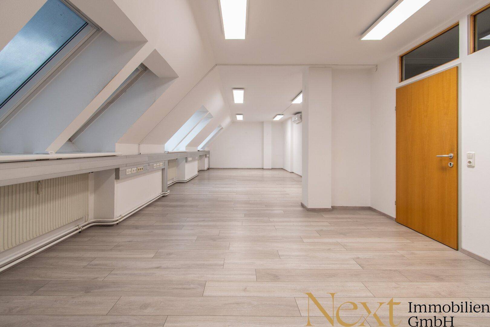 Langer, heller Büroraum mit mehreren Dachfenstern und modernem Laminatboden, ideal für Arbeitsplätze.