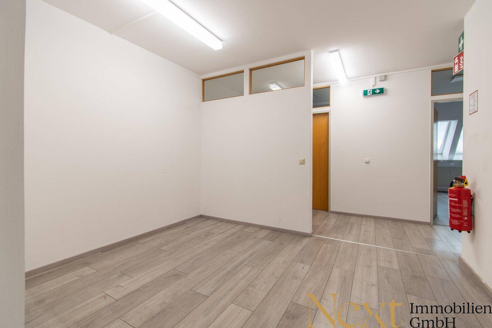 Flur oder offener Bürobereich mit Holztür, Oberlichtern und Laminatboden, mit Brandschutzhinweisen.