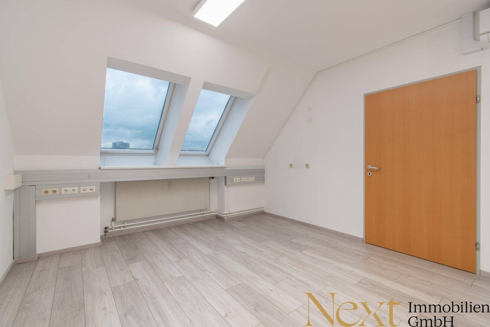 Detailansicht eines Bürobereichs mit zwei großen Dachfenstern, Heizkörpern und einer Holztür.