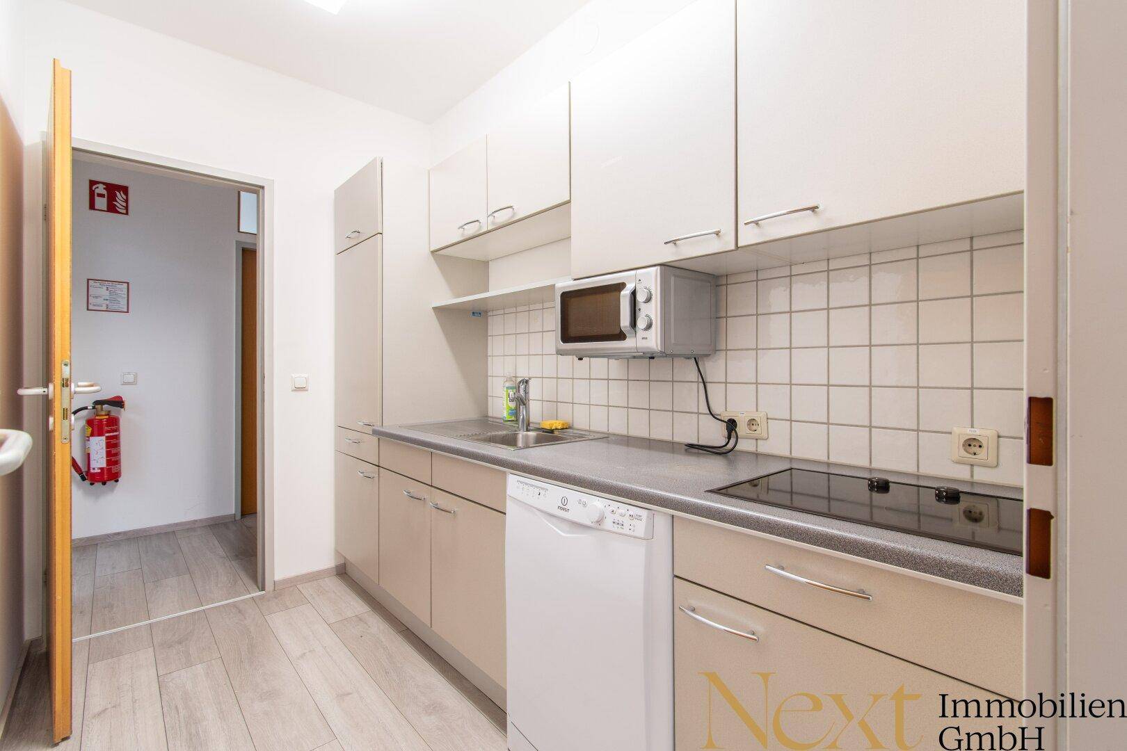 Funktionale Küche mit weißen Schränken, Spülmaschine, Mikrowelle und Induktionskochfeld.