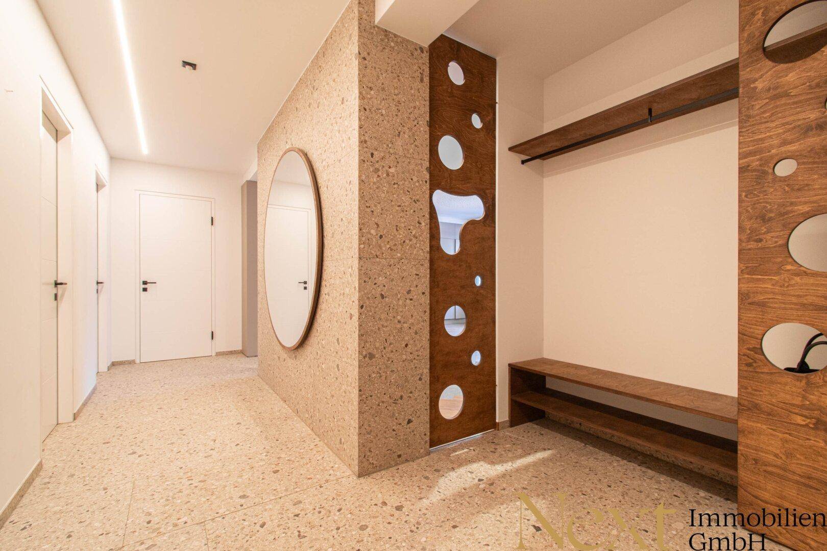 Heller Eingangsbereich mit Terrazzoboden, großem Spiegel und dekorativer Holzwand.