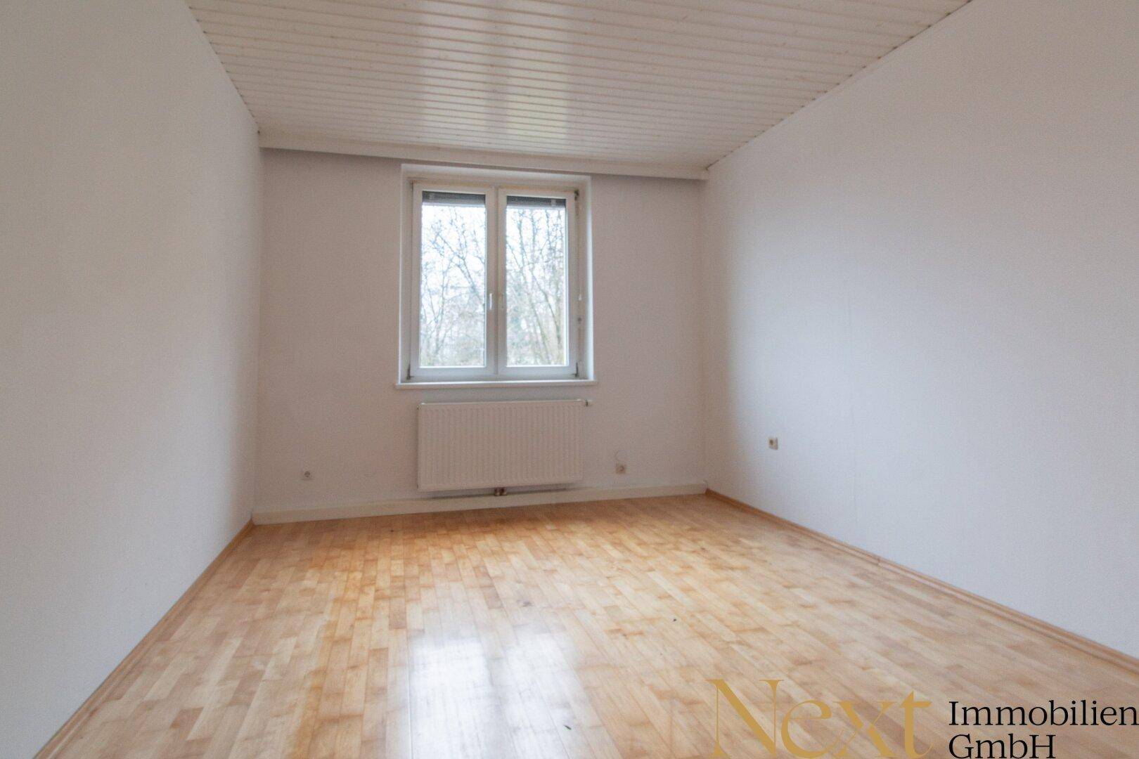 Helles Schlafzimmer mit Holzboden, Fenster und weißer Deckenverkleidung, bietet eine ruhige Atmosphäre.