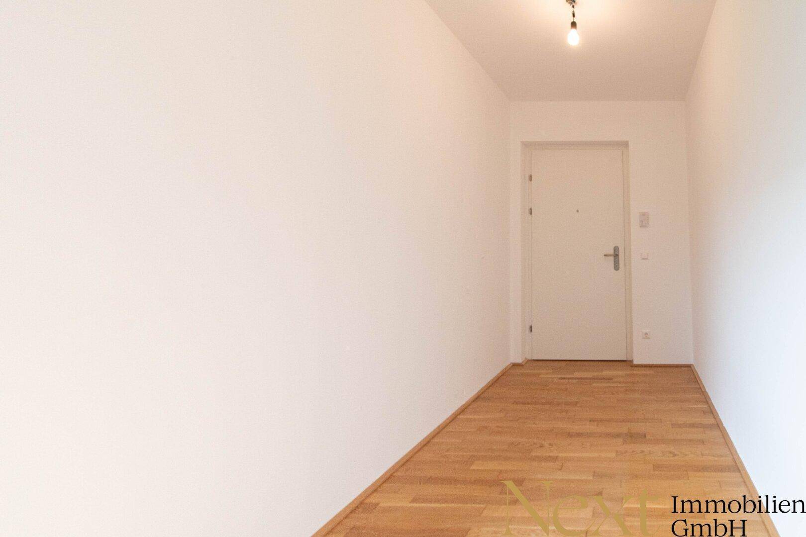 Heller, leerer Flur mit Parkettboden und weiß gestrichenen Wänden.