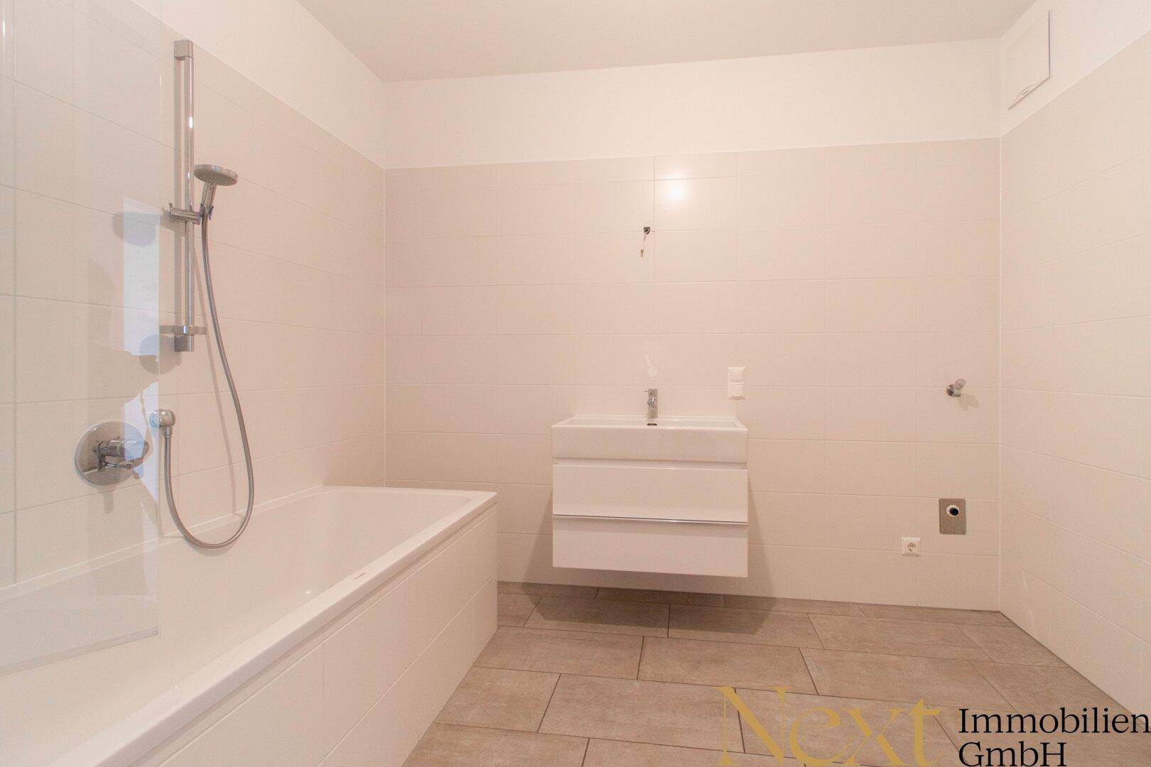 Helles Badezimmer mit Badewanne, Einzelwaschbecken und modernen Fliesen.
