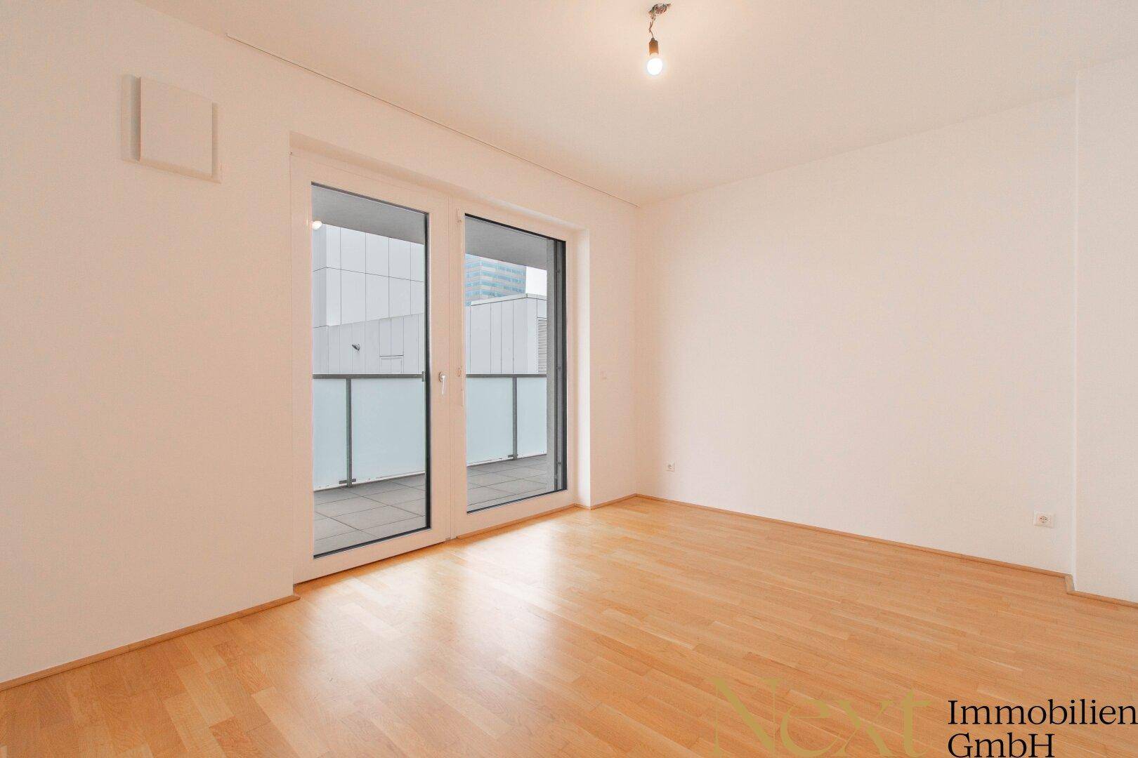 Leeres Schlafzimmer mit hellem Parkettboden und direktem Zugang zum Balkon.