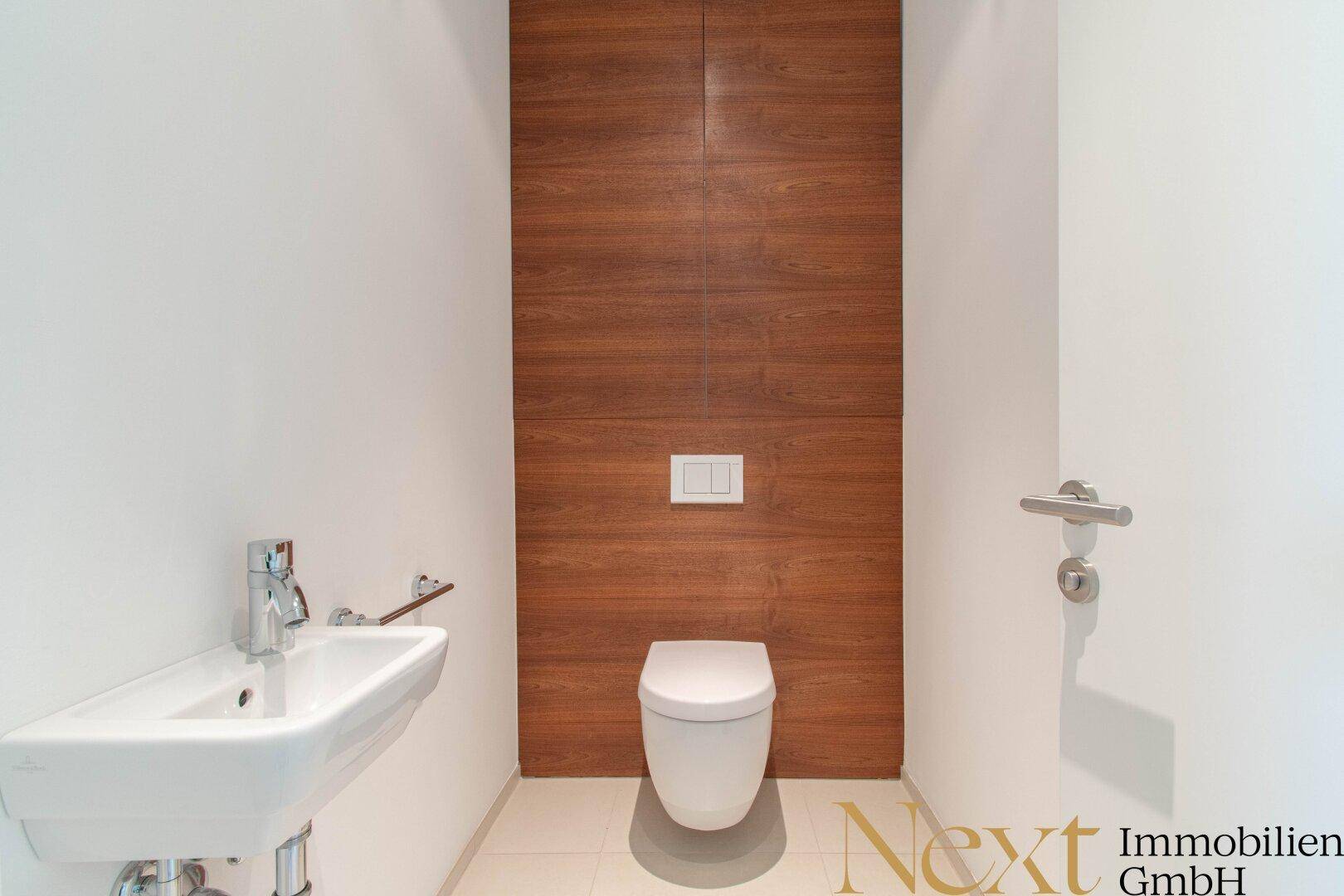 Gäste-WC mit wandhängendem WC, kleinem Waschbecken und einer eleganten Holzwandverkleidung.