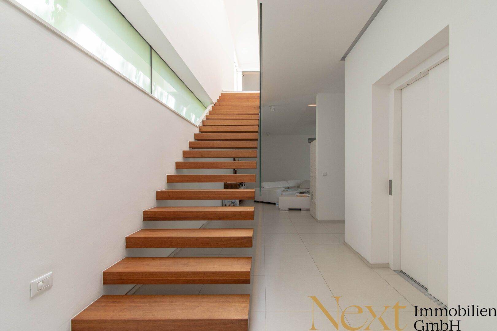 Elegante Holztreppe mit Glasgeländer, die vom hellen Flur in die obere Etage führt.