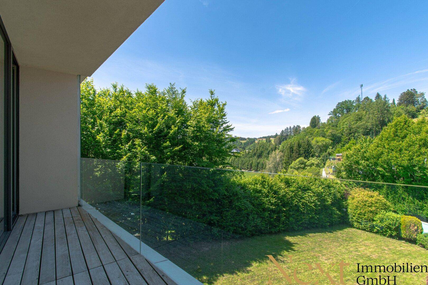 Balkon mit Glasgeländer und Holzdeck, der einen weiten Blick über die grüne Landschaft bietet.