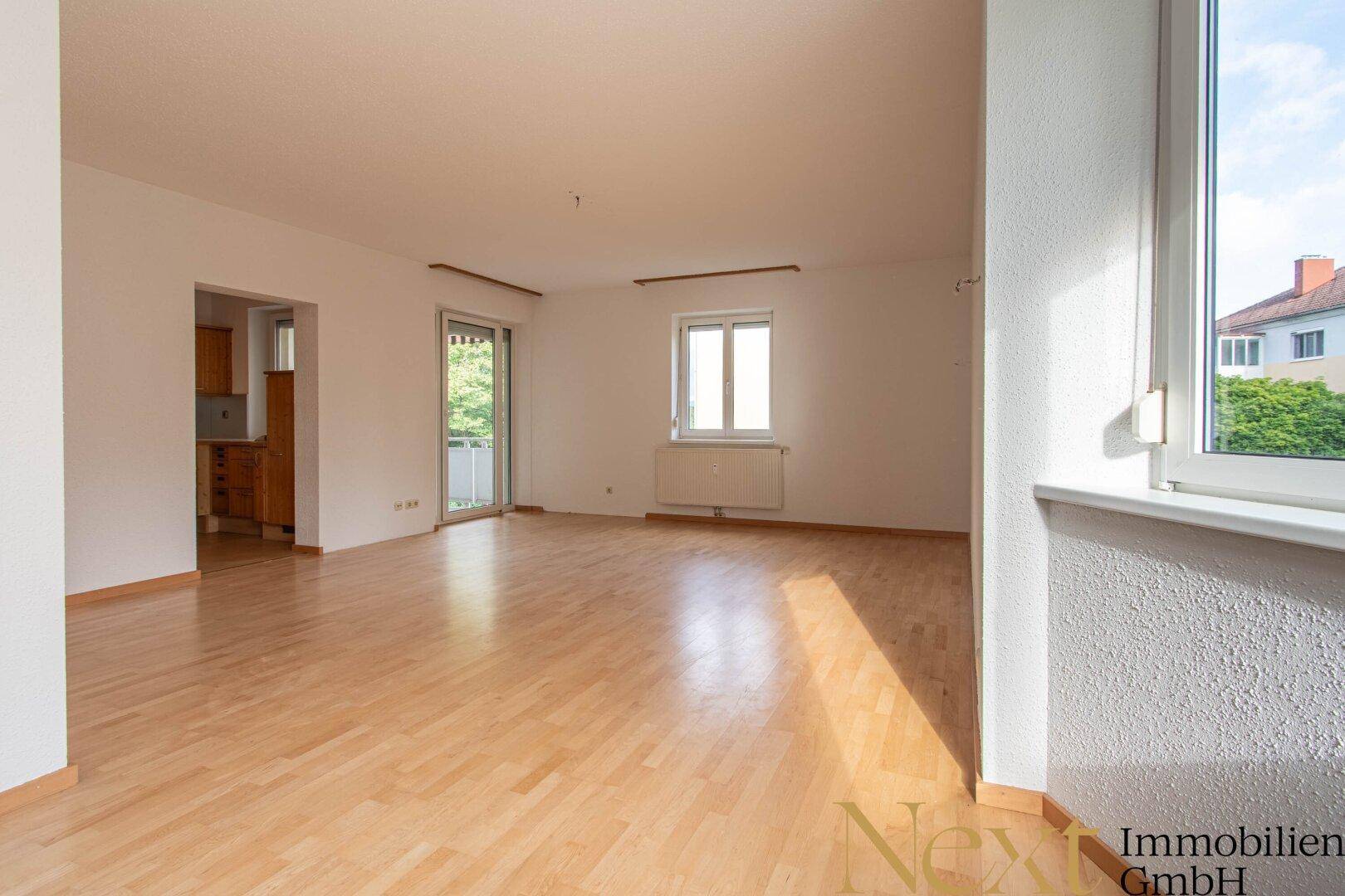 Helles Wohnzimmer mit Echtholzparkett, großen Fenstern und Zugang zum Balkon.
