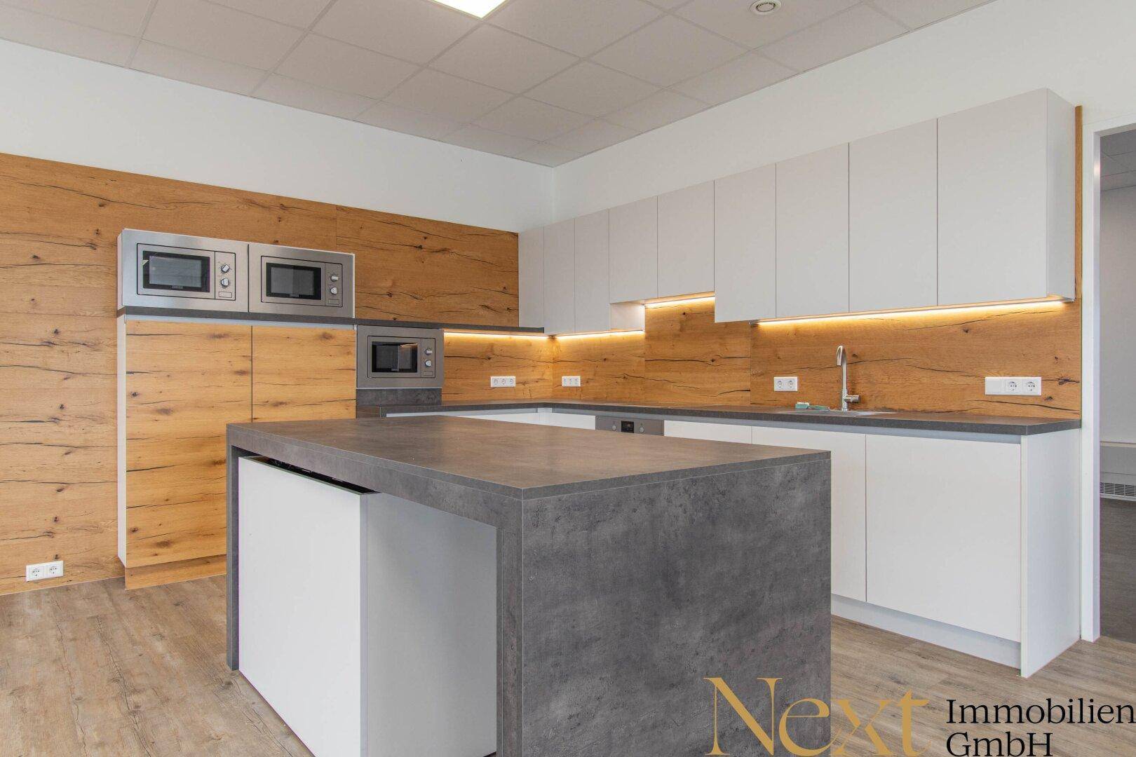 Moderne Einbauküche mit weißen Schränken, Holzverkleidung und Kücheninsel in einem Büro.