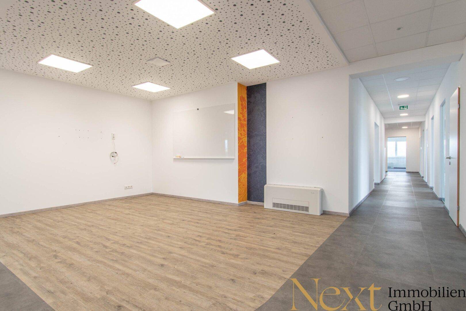 Helles Büro mit Holzoptik-Laminatboden, weißer Tafel und Blick in einen modernen Flur.