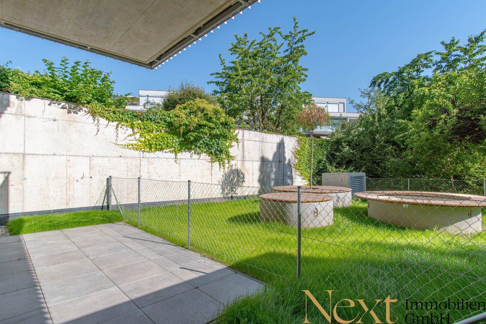 Gemeinschaftsgarten mit Rasenfläche und runden Sitzgelegenheiten aus Holz und Beton.