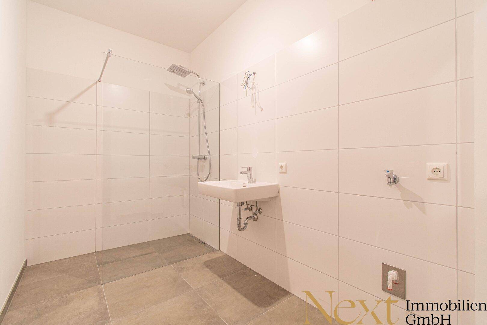 Modernes Badezimmer mit begehbarer Dusche, Waschbecken und weißen Fliesen an den Wänden.