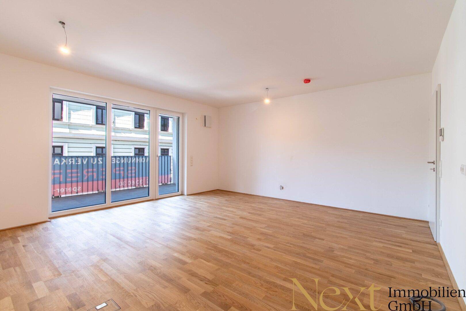 Geräumiges Zimmer mit hellem Parkettboden und großen Fenstern, die viel Tageslicht hereinlassen.