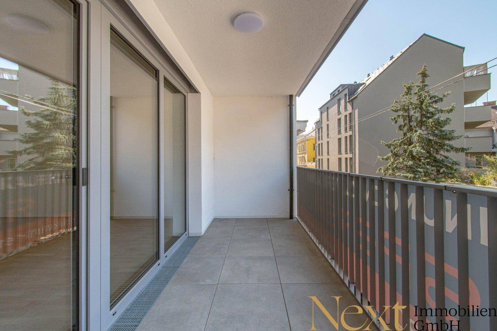 Geräumiger Balkon mit Fliesenboden und Blick auf die umliegenden Gebäude und Bäume.