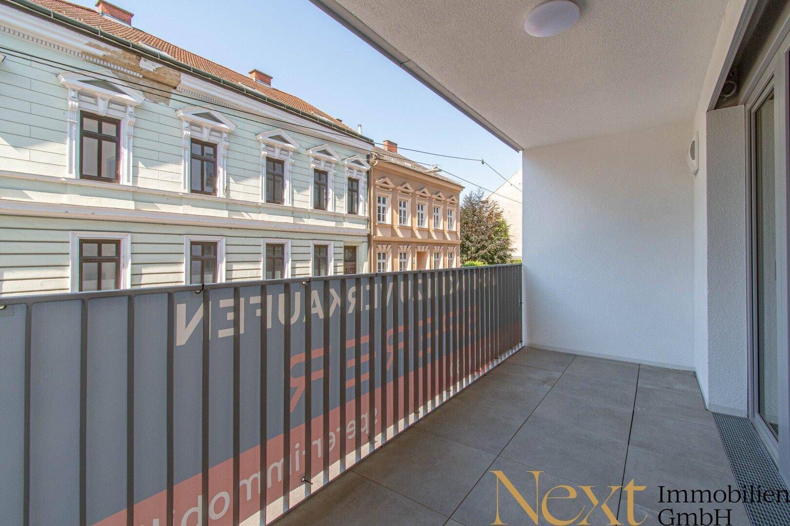 Balkon mit Fliesenboden und Blick auf eine charmante Straße mit historischen Gebäuden.