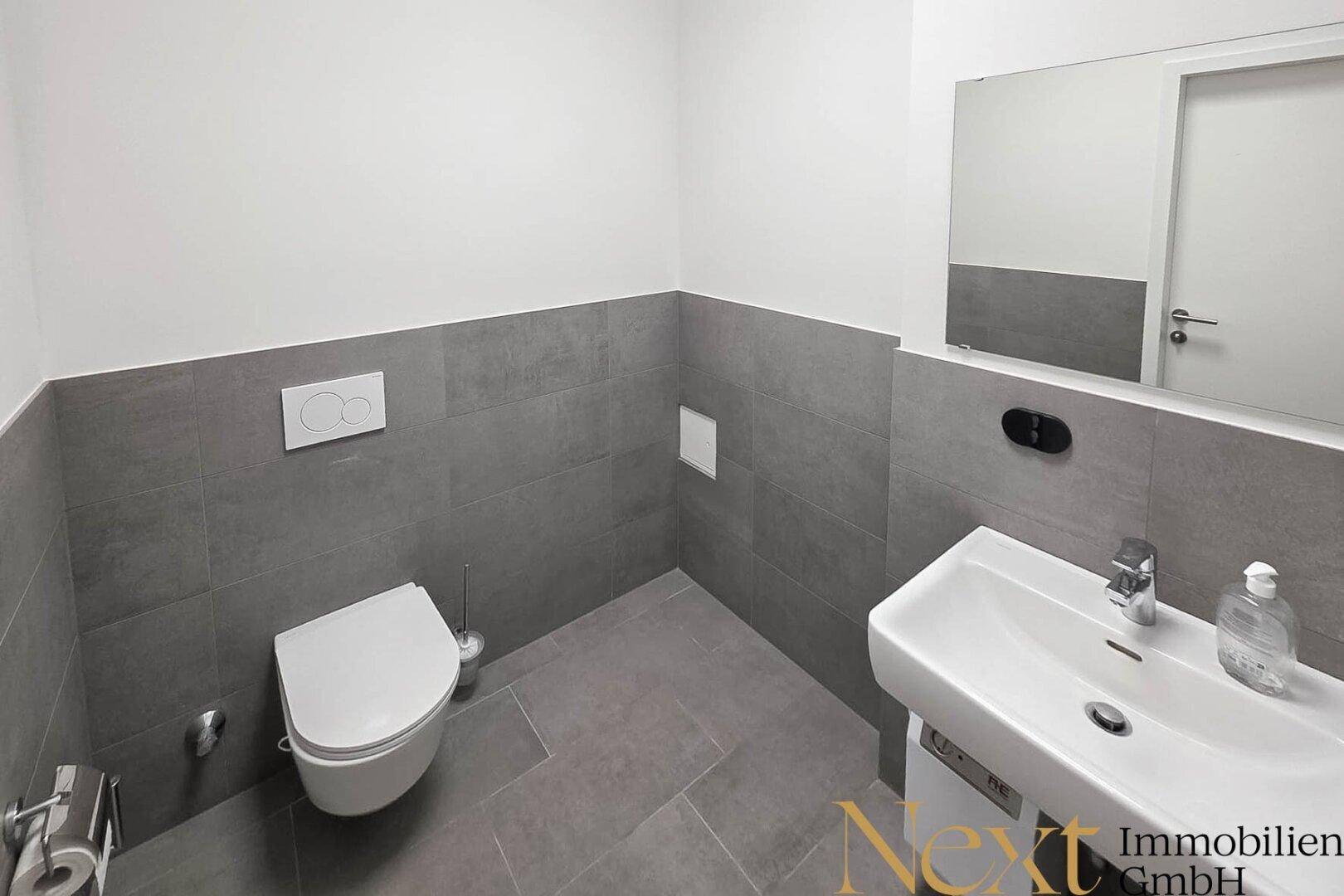Modernes Gäste-WC mit stilvollen grauen Fliesen an Wänden und Boden, ausgestattet mit Wand-WC und Waschbecken.