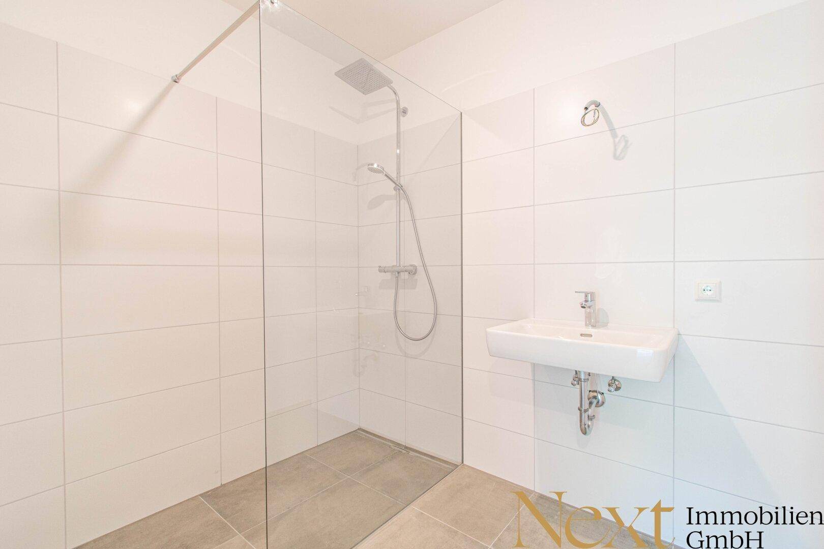 Modernes Badezimmer mit weißen Fliesen, begehbarer Dusche und Wandwaschbecken.