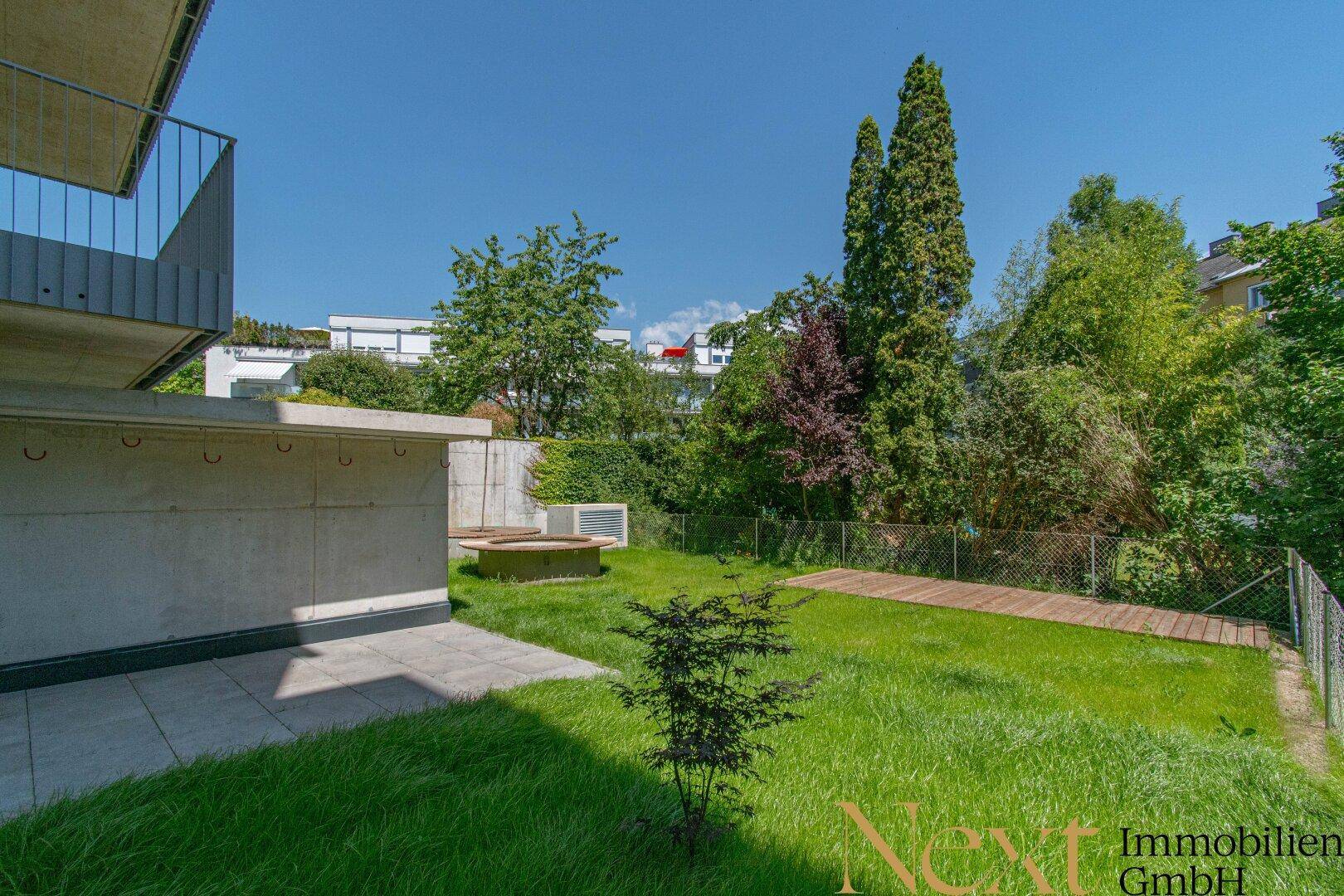 Privater Gartenbereich mit gepflasterter Terrasse, Rasenfläche und üppiger Bepflanzung.