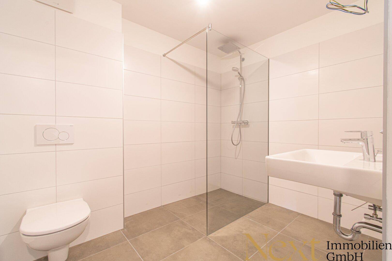 Modernes Badezimmer mit weißen Fliesen, ebenerdiger Dusche und wandhängendem WC.