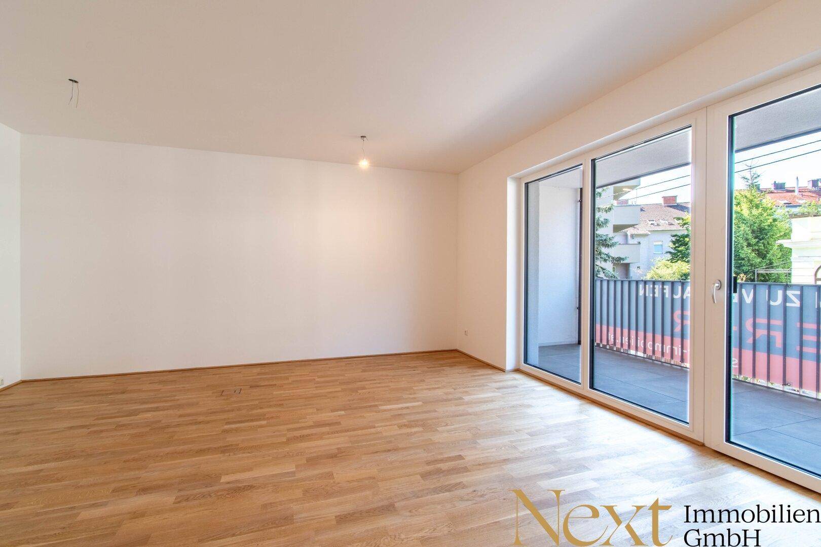 Heller, leerer Wohnraum mit Parkettboden und großen Schiebetüren zum Balkon.