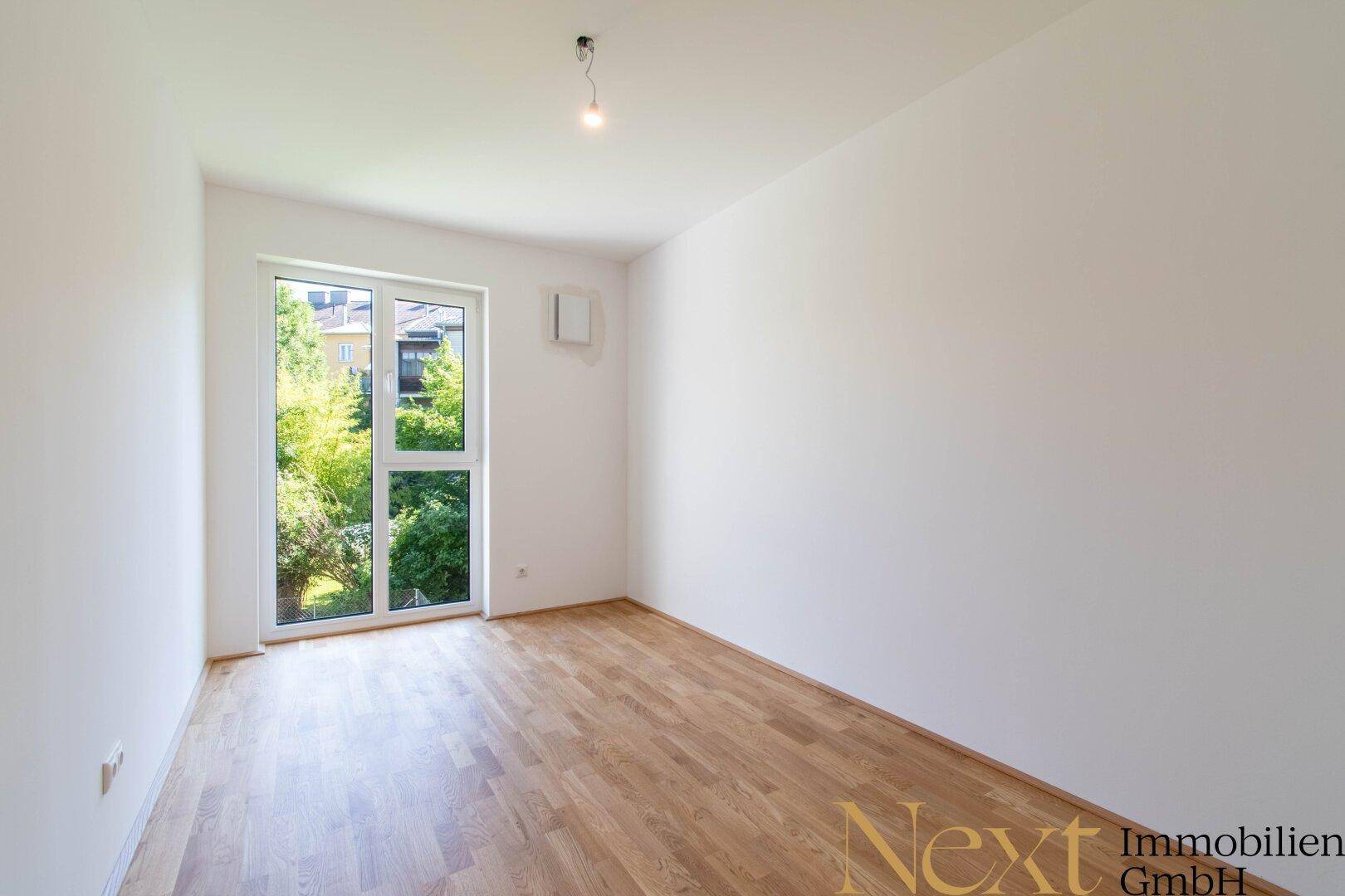 Helles Zimmer mit Parkettboden und Fenster mit Blick ins Grüne, ideal als Schlaf- oder Arbeitszimmer.