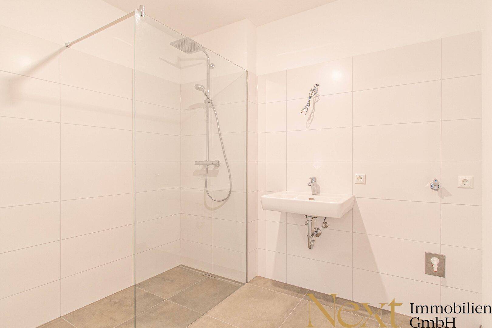 Modernes Badezimmer mit weiß gefliesten Wänden, ebenerdiger Dusche und Waschbecken.