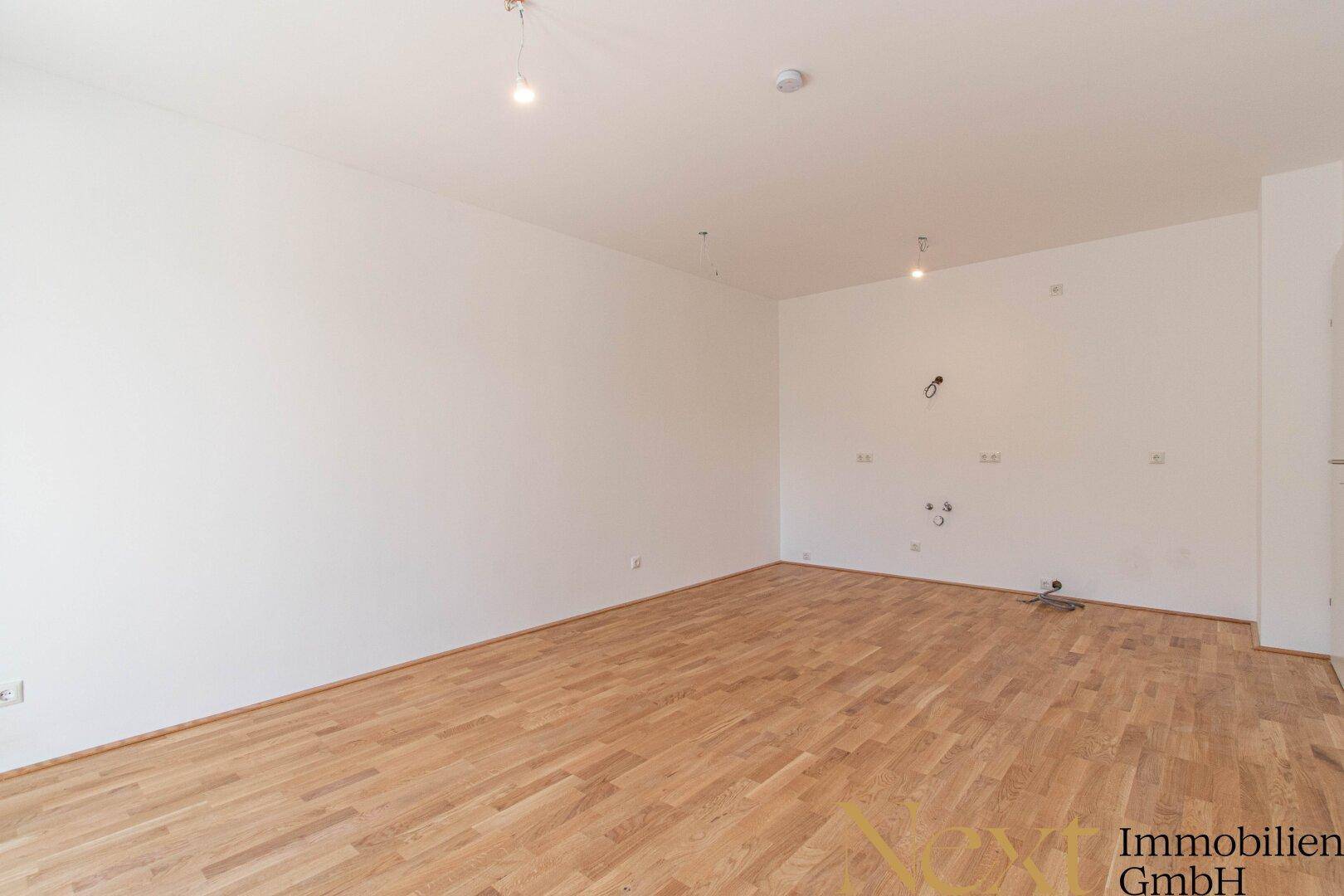 Geräumiges, leeres Zimmer mit Parkettboden und weißen Wänden, bereit für die Einrichtung.