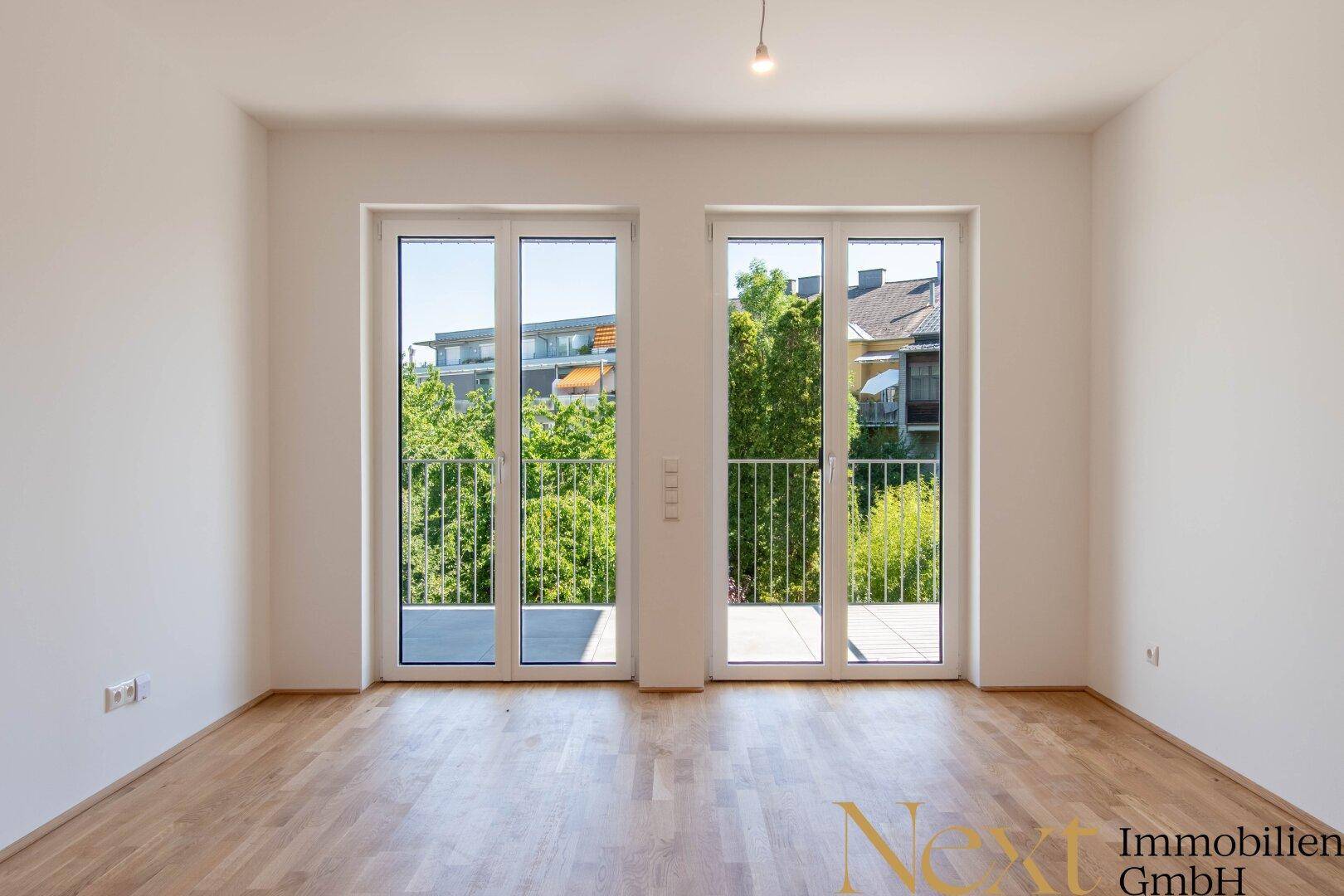 Lichtdurchflutetes Zimmer mit Parkettboden und zwei großen Fenstertüren zu französischen Balkonen.