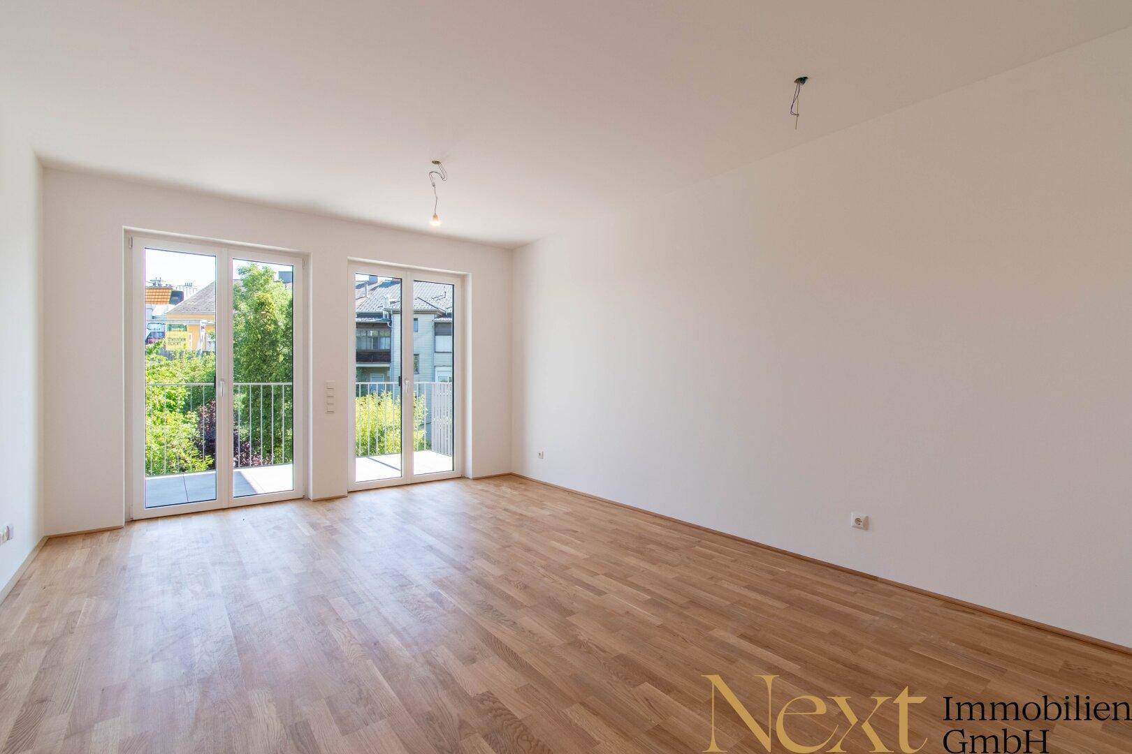 Helles, leeres Zimmer mit Parkettboden und Zugang zu einem französischen Balkon.