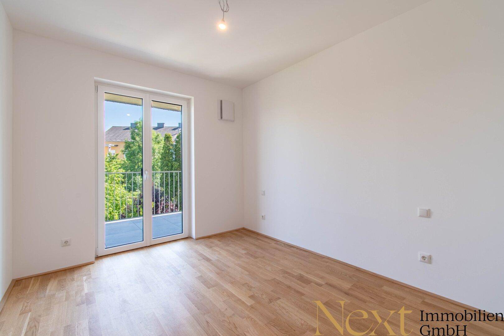 Leeres Schlafzimmer mit Parkettboden und Zugang zu einem französischen Balkon.