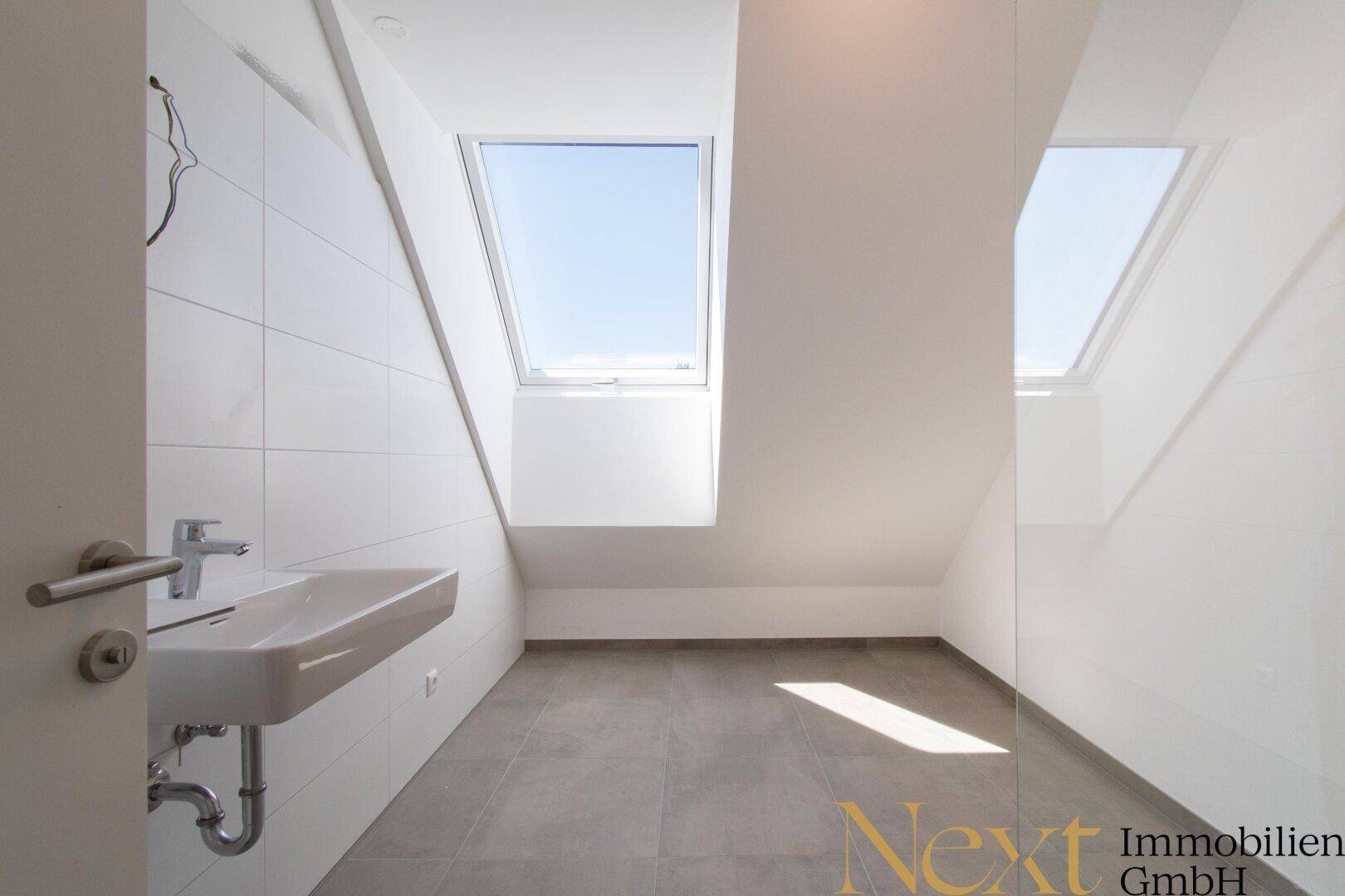 Modernes Badezimmer mit weißen Fliesen, grauem Boden und zwei Dachfenstern für natürliches Licht.