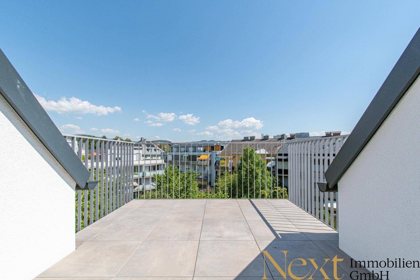 Weitläufige Dachterrasse mit Fliesenboden und Panoramablick über die Dächer und grüne Umgebung.