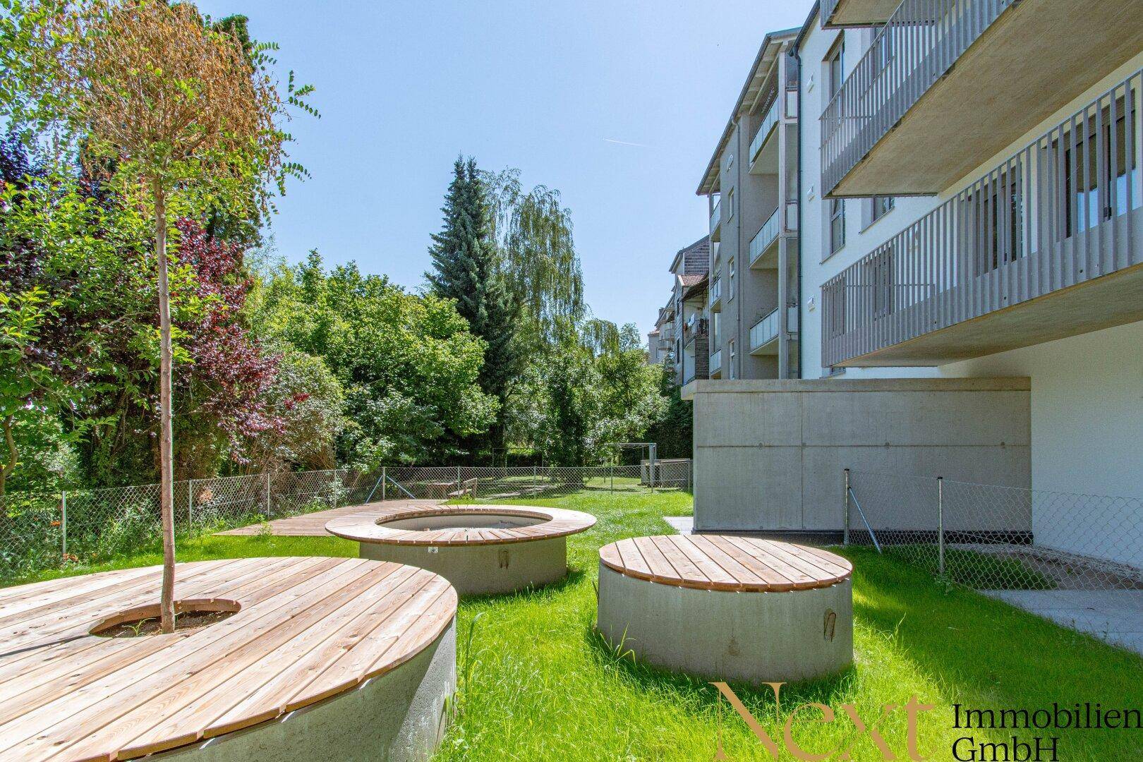 Gemeinschaftlicher Gartenbereich mit Rasenfläche und modernen Holz-Sitzgelegenheiten im Freien.