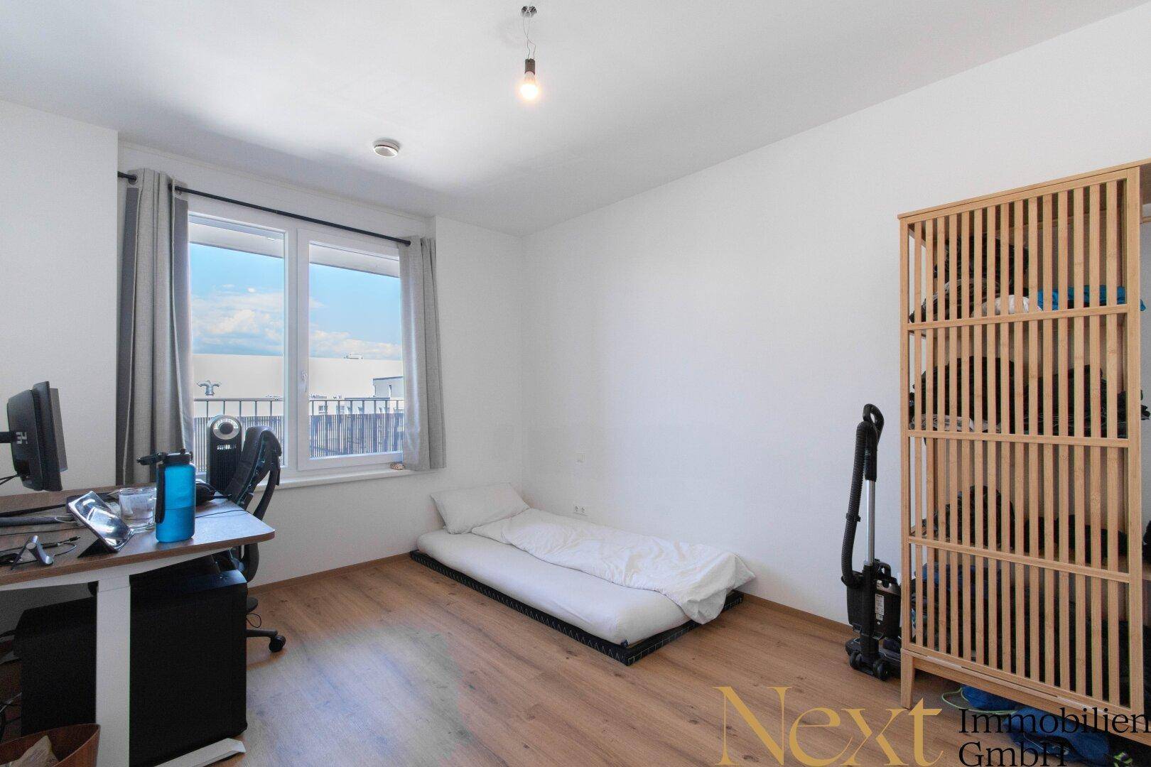 Schlafzimmer mit einfachem Bett, Schreibtisch und Fenster, das viel Tageslicht hereinlässt.