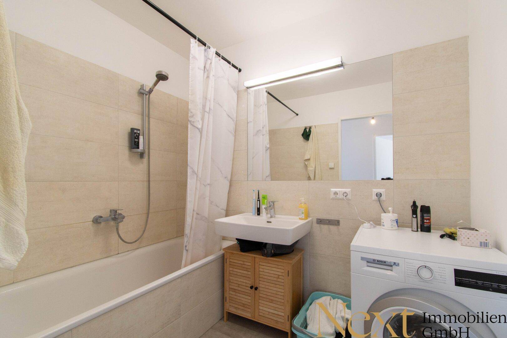 Badezimmer mit Badewanne inklusive Duschfunktion, Waschbecken und Waschmaschine.