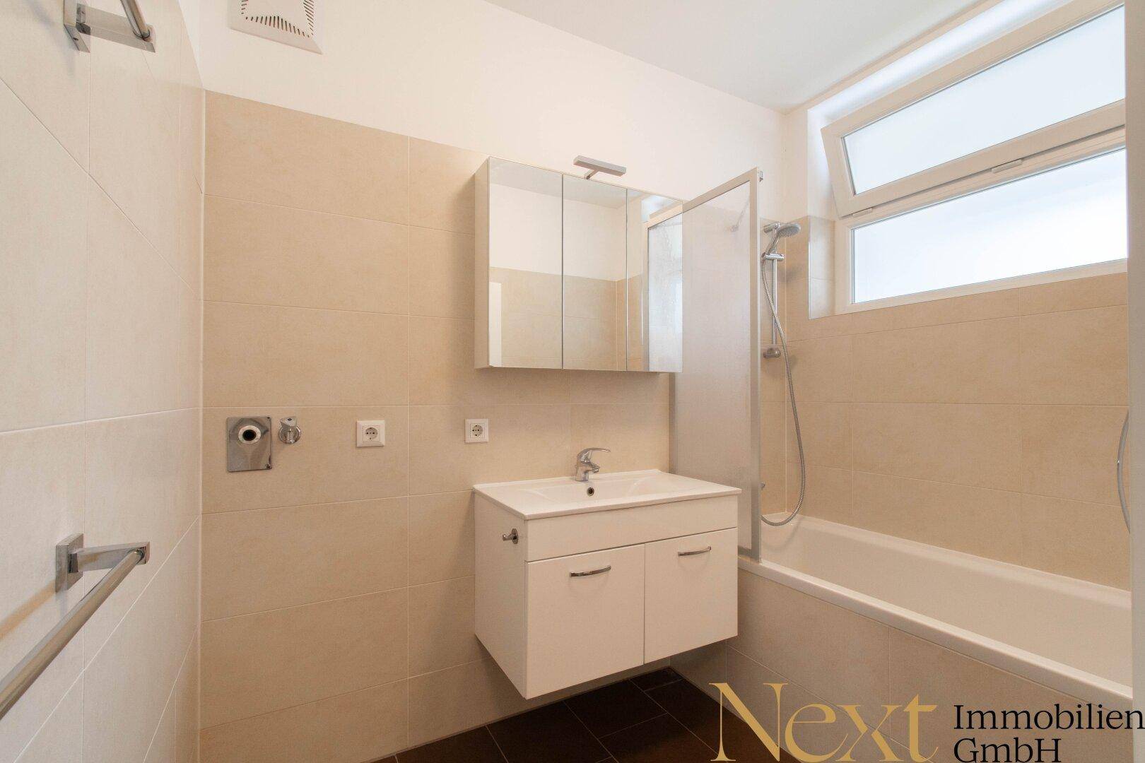Modernes Badezimmer mit beigefarbenen Fliesen, Badewanne mit Duschfunktion und Fenster.